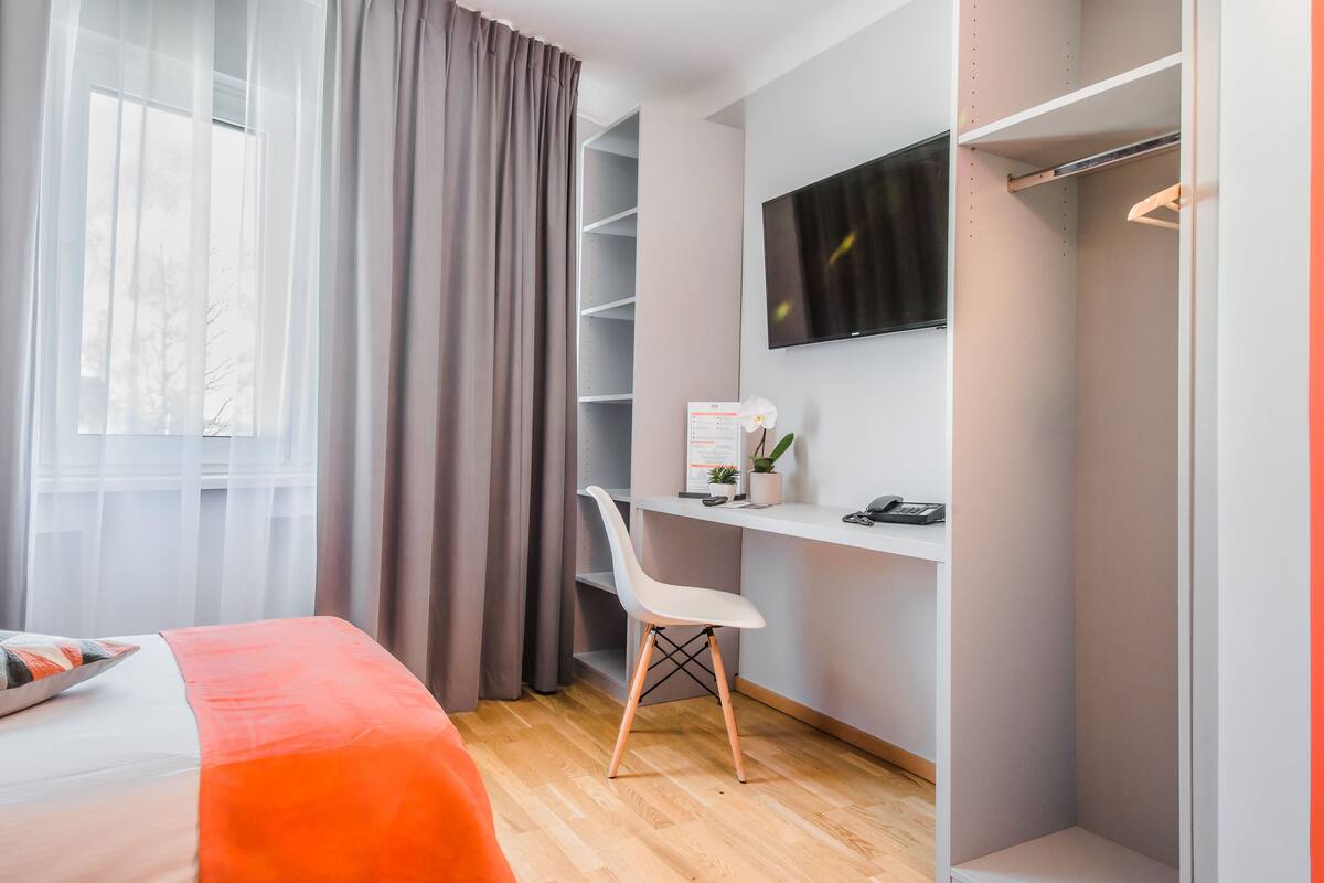 A modern bedroom with a bed, a desk, a chair, a TV, and a wardrobe.