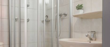 Un baño con ducha de vidrio, lavamanos blanco y espejo sobre él.