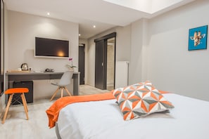 A modern hotel room with a bed, a desk, a chair, a television, and a door leading to a bathroom.