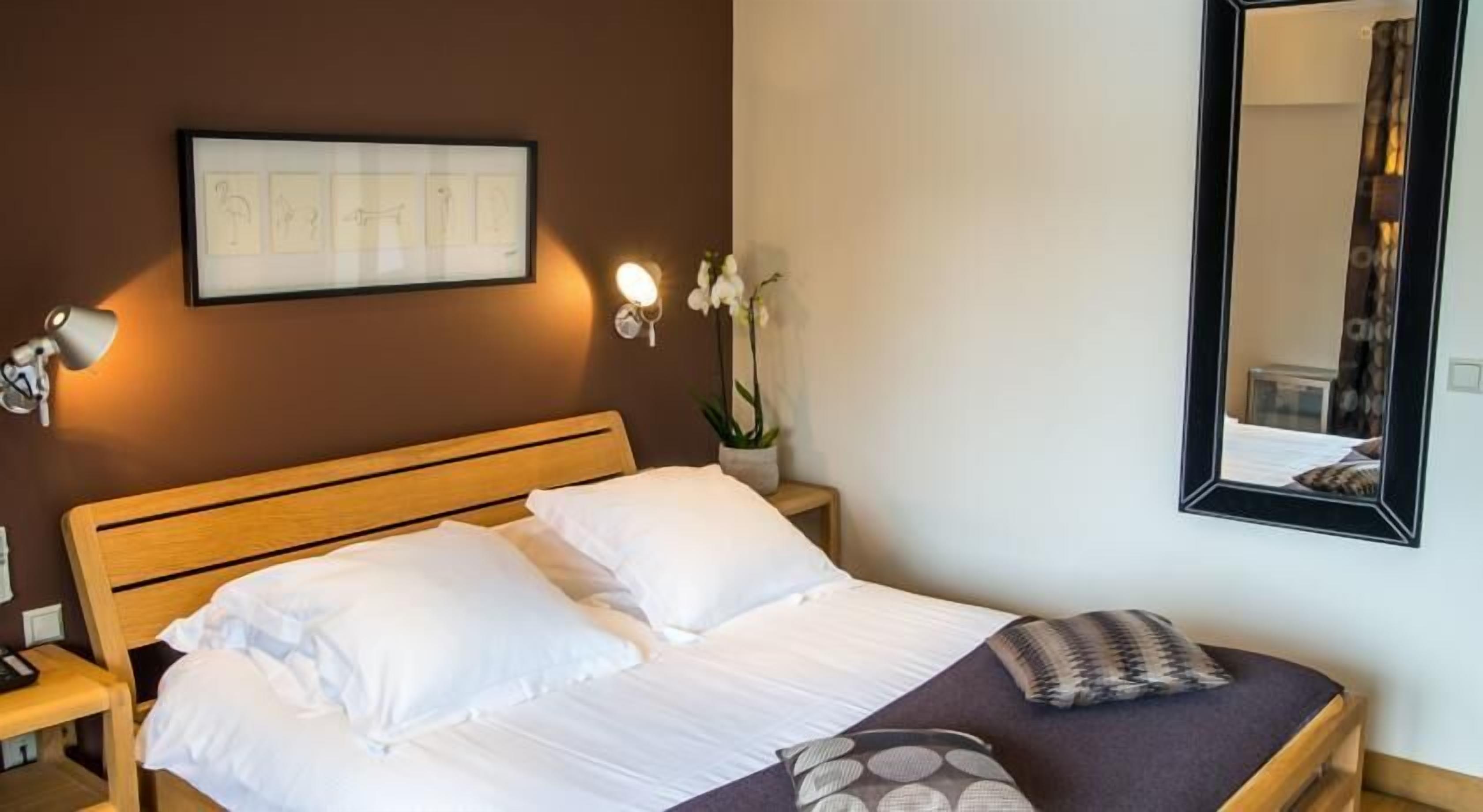A neatly made bed with white linens, a wooden headboard, and a single decorative pillow.