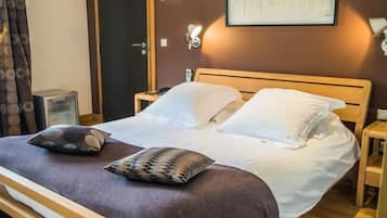 A neatly made bed with white linens and two decorative pillows, a bedside table with a lamp, and a wall-mounted light fixture.