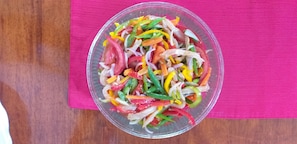 Un saladier en verre transparent rempli d’une salade de légumes colorée, posé sur un tissu rose.
