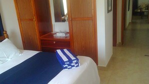 Ein Hotelzimmer mit einem Bett, einem Nachttisch aus Holz, einem Spiegel und einem durch eine offene Tür einsehbaren Badezimmer.