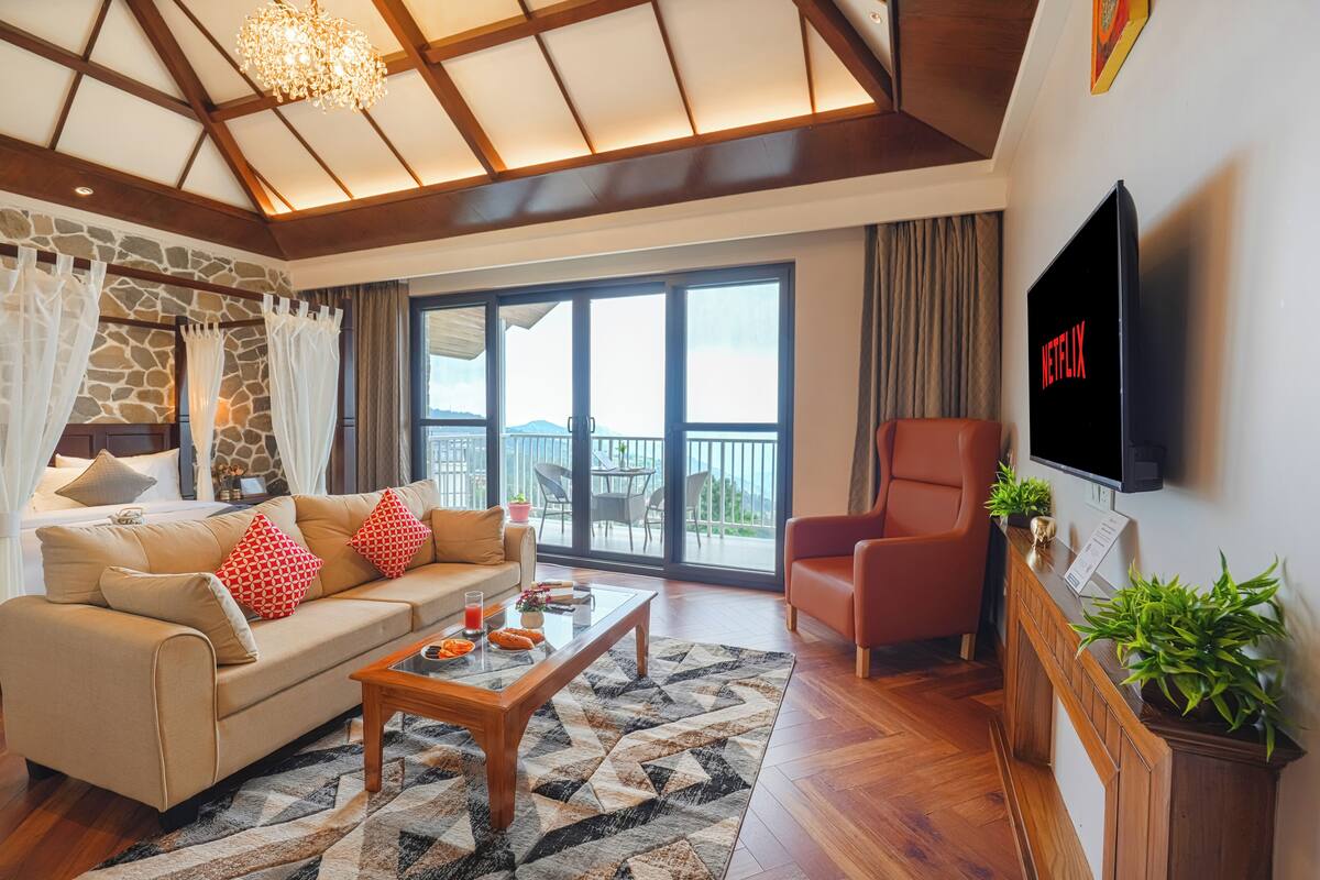 A spacious living room with a sofa, armchair, and a coffee table. A TV mounted on the wall displays the Netflix logo.