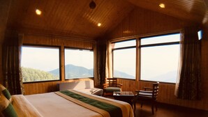 Een slaapkamer met een groot bed, een stoel, een klein tafeltje en grote ramen met uitzicht op bergen.