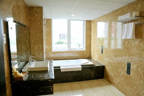 A modern bathroom with a large bathtub, a sink, and a shower. There is a window providing natural light and a view of the outside.