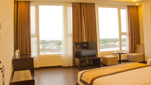 A hotel room with a large bed, a television, a small table, and a chair. - International Hotel (Can Tho)