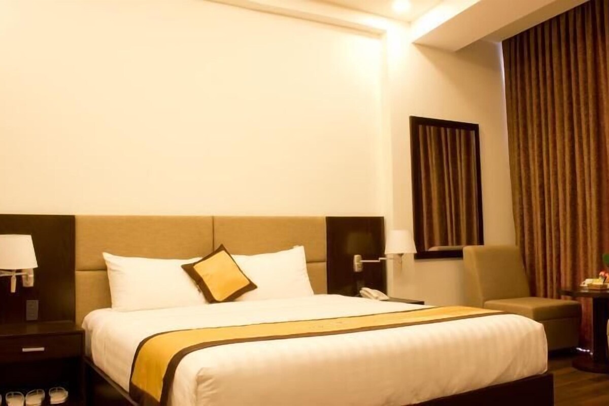 A hotel room with a bed, a chair, a nightstand, a lamp, and a window with curtains.