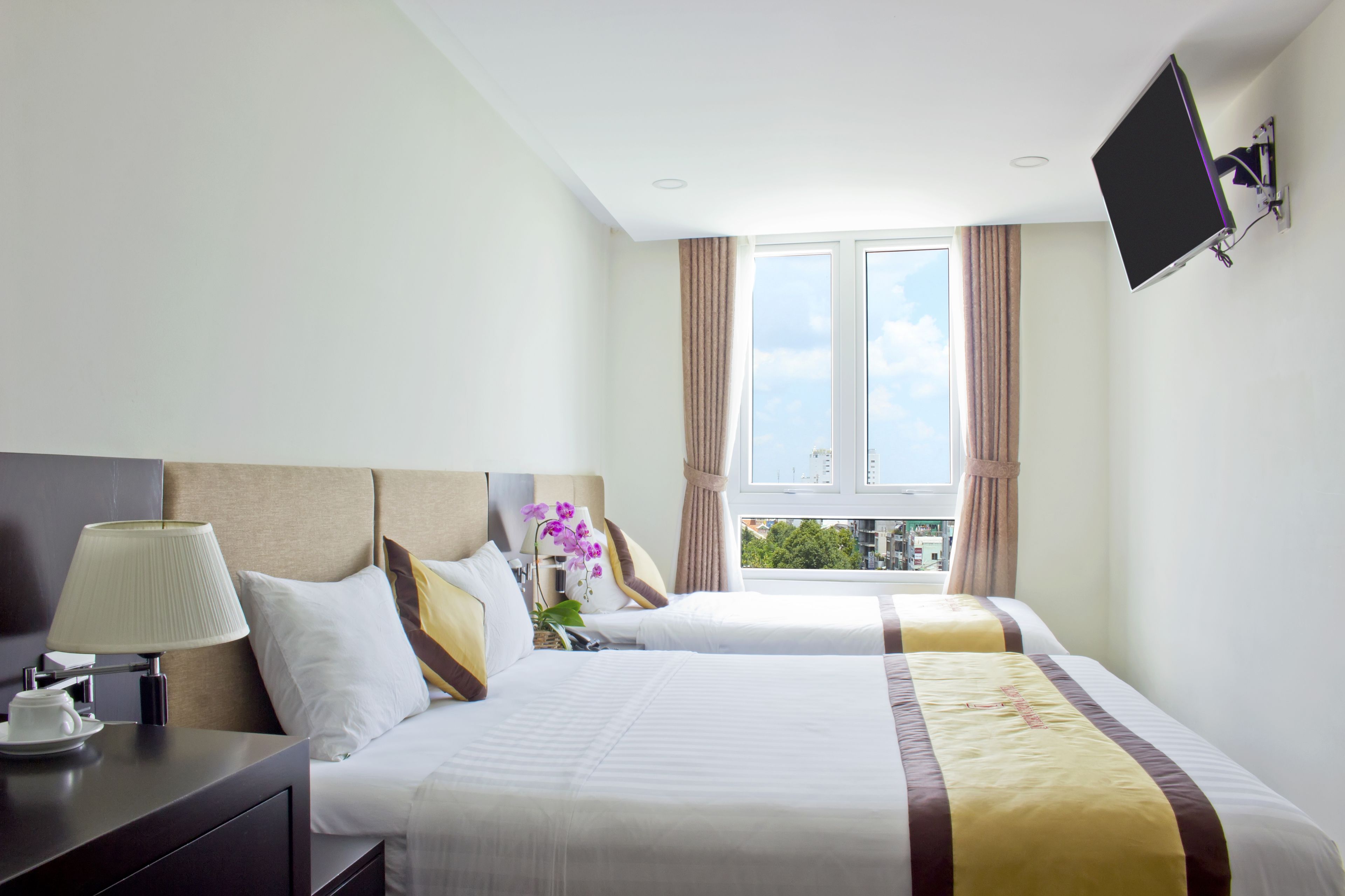 A hotel room with two beds, a TV mounted on the wall, and a window with curtains.