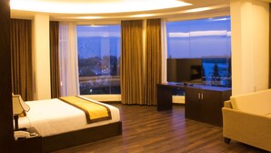 A modern hotel room with a large bed, a desk, and a sofa. There is a large window with a view of the city at night. - International Hotel (Can Tho)