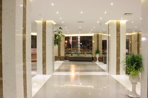 A spacious lobby with marble columns, a seating area, and potted plants.