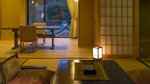 Una habitación japonesa tradicional con suelo de tatami, una mesa baja con cojín, una silla y un puertas correderas con diseño de cuadrícula.