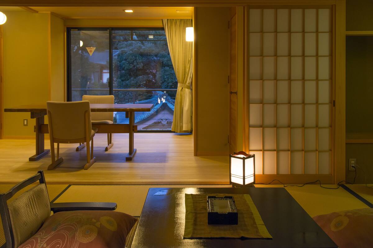 A traditional Japanese room with tatami flooring, a low table with a cushion, a chair, and a sliding door with a grid pattern.