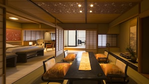 Una habitación japonesa tradicional con suelo de tatami, una mesa baja con cojines, una cama futón, puertas correderas y vistas a un jardín.