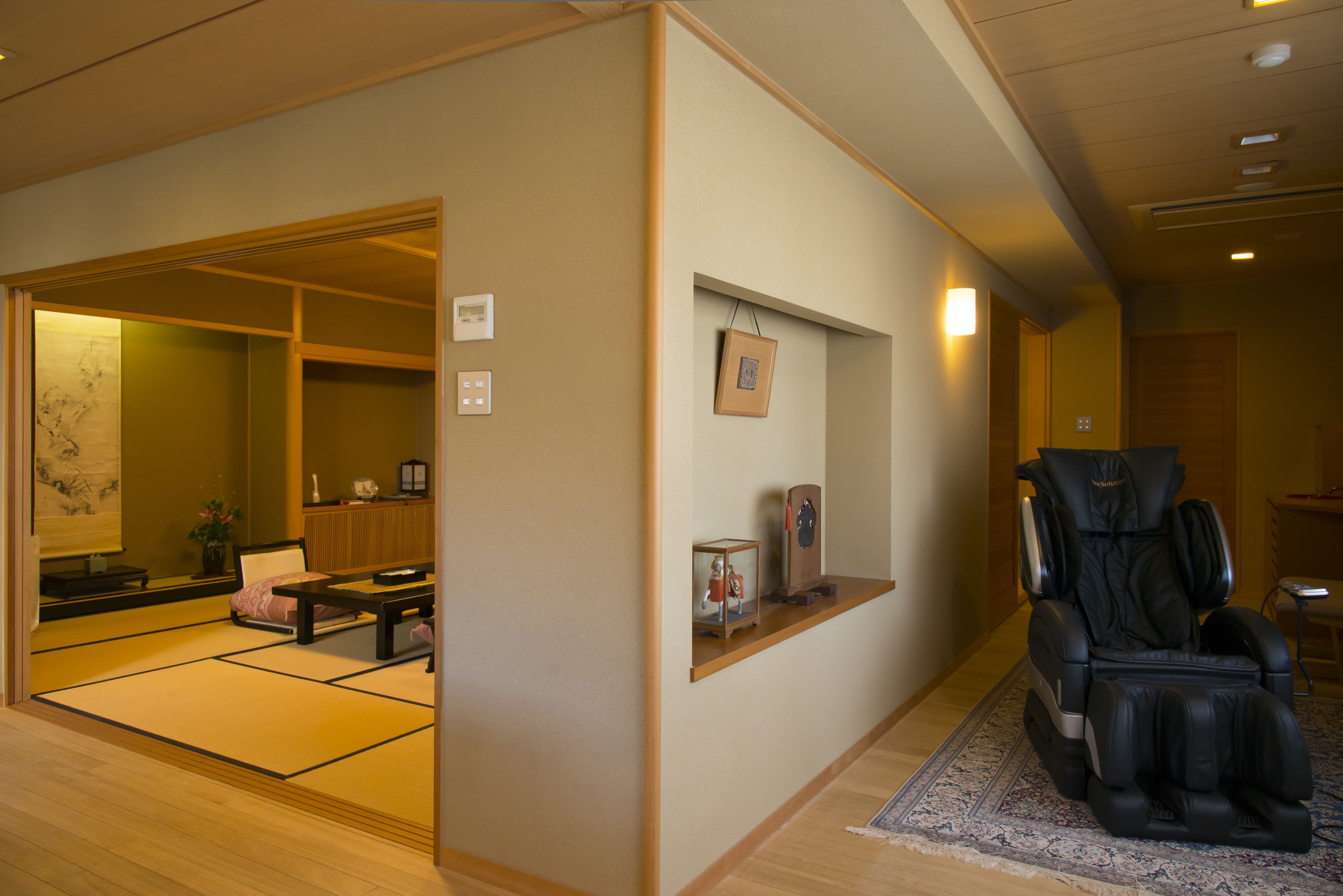 A traditional Japanese room with tatami flooring, a tatami mat arrangement, a massage chair, and a small shelf with decorative items.