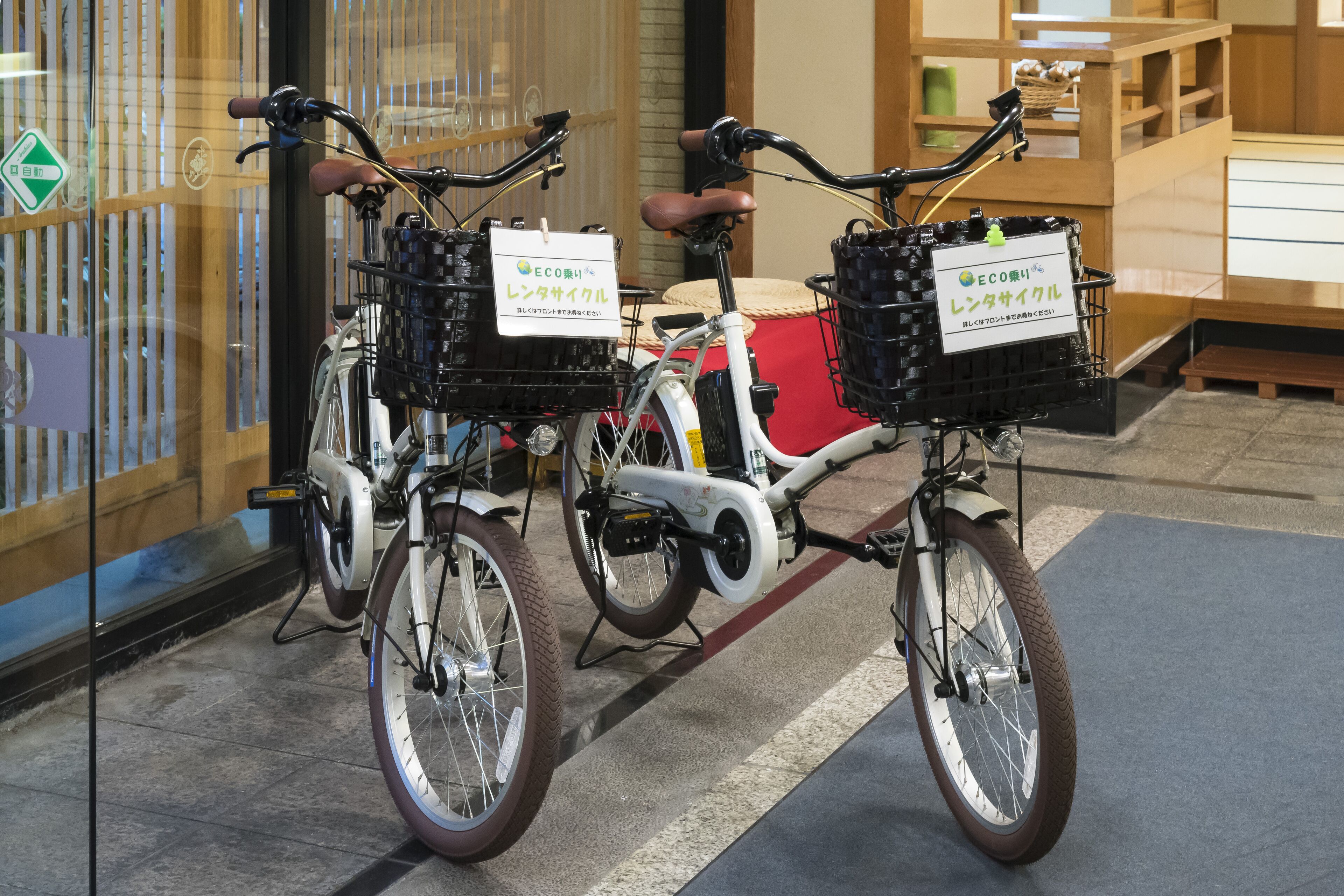 Twee fietsen met mandjes en borden, geparkeerd voor een gebouw met houten inrichting.