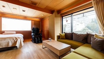 A modern hotel room with a bed, a sofa, a massage chair, and a window with a view of buildings.