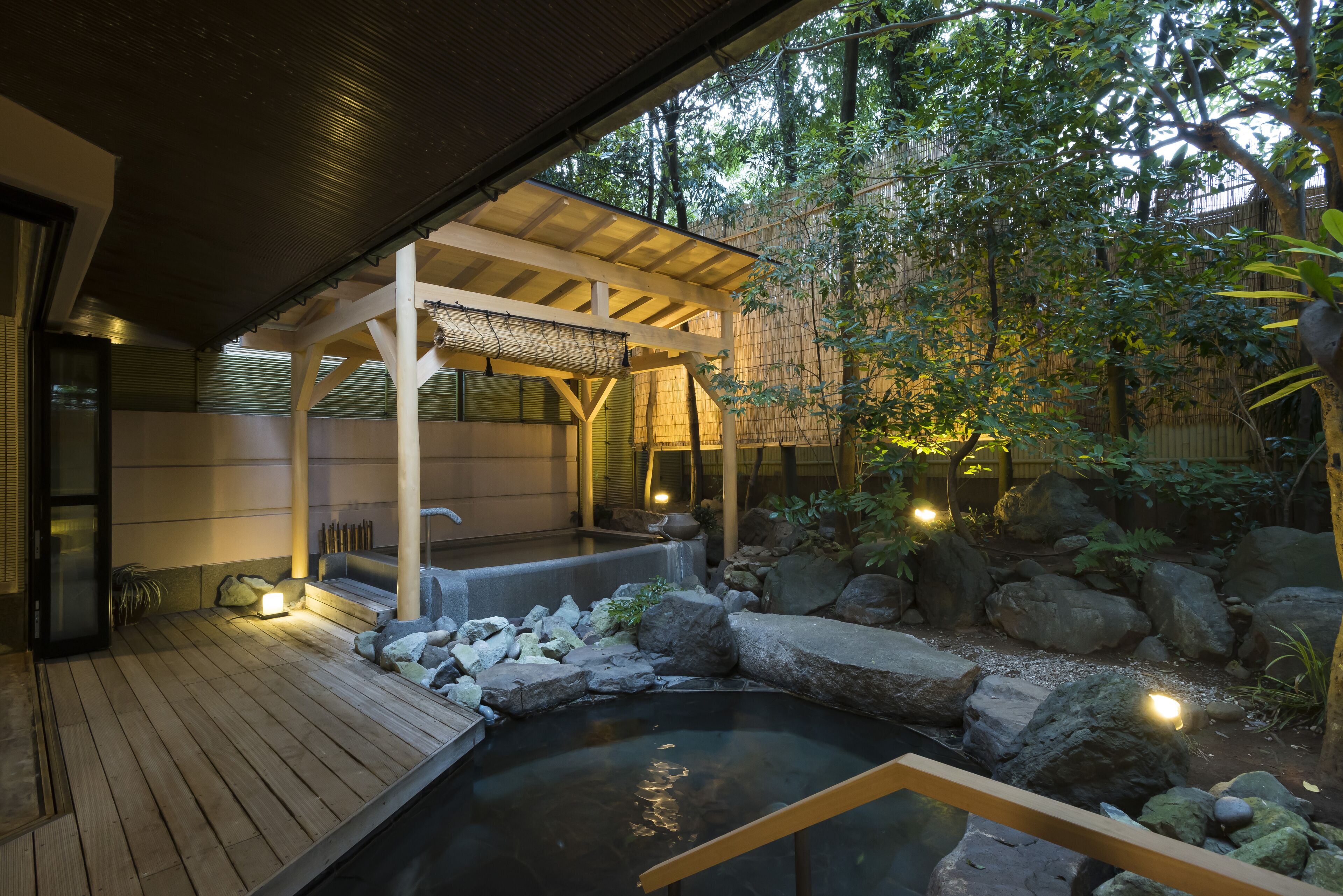 Un jardín japonés tradicional con terraza de madera, aguas termales y una zona de estar cubierta.