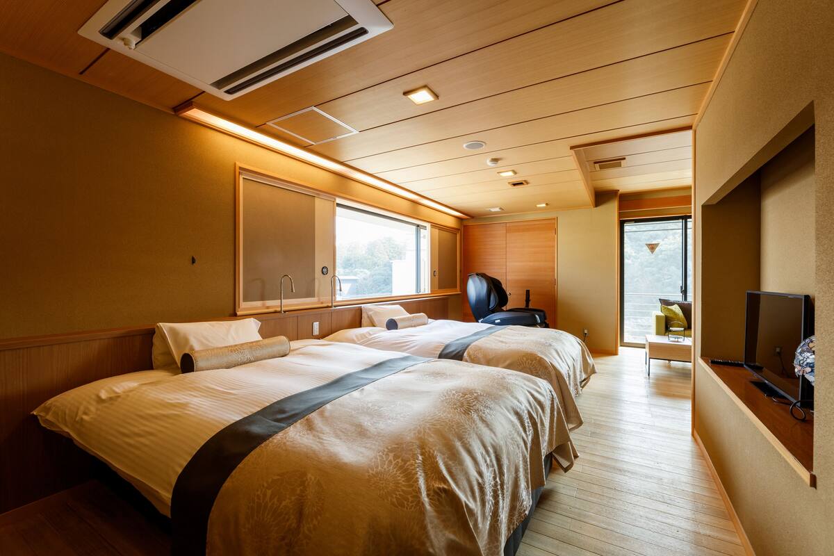 A hotel room with two beds, a TV, and a window with a view.
