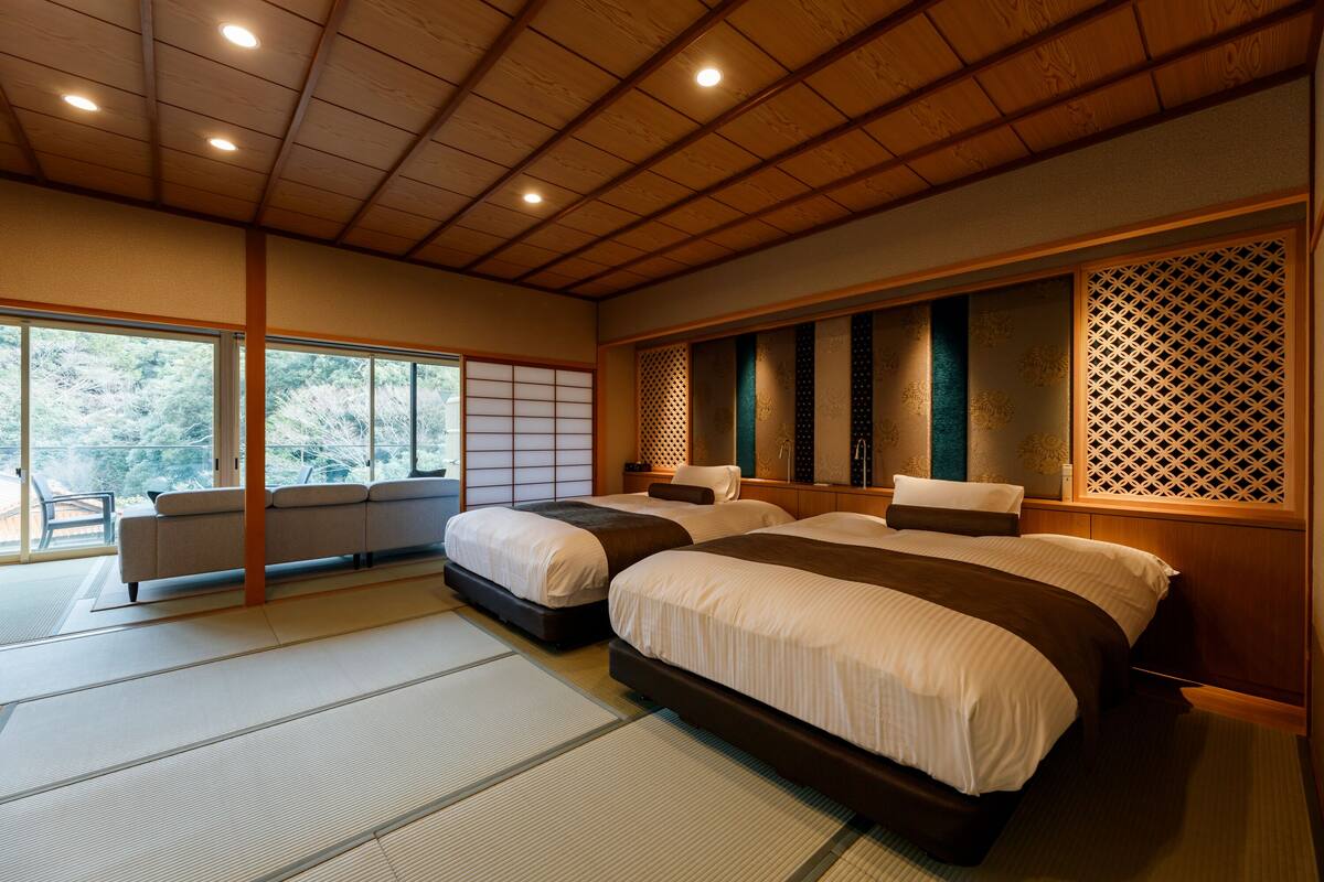 A traditional Japanese-style bedroom with tatami flooring, two beds, a sofa, and a sliding shoji screen.