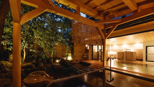 Un jardín interior tranquilo con terraza de madera, pila de piedra y vistas al cielo nocturno.