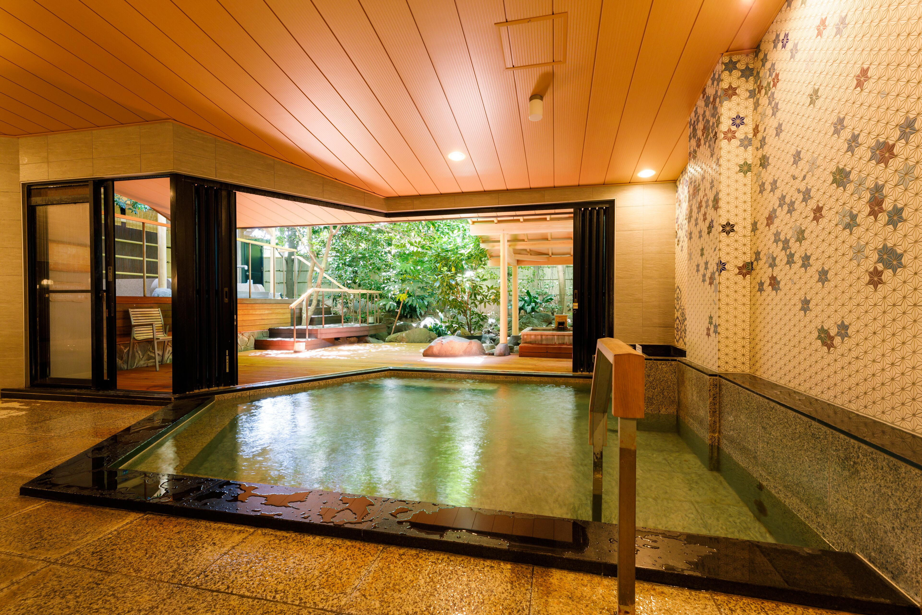 A modern indoor pool with a glass barrier, wooden ceiling, and patterned walls.