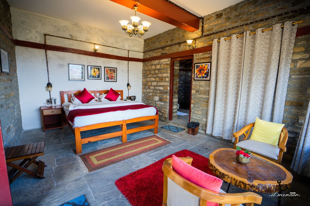 Ein Schlafzimmer mit einem hölzernen Bett, roten Kissen, einem Nachttisch, einem Holzstuhl, einem runden Holztisch mit einer Vase und einem roten Teppich.