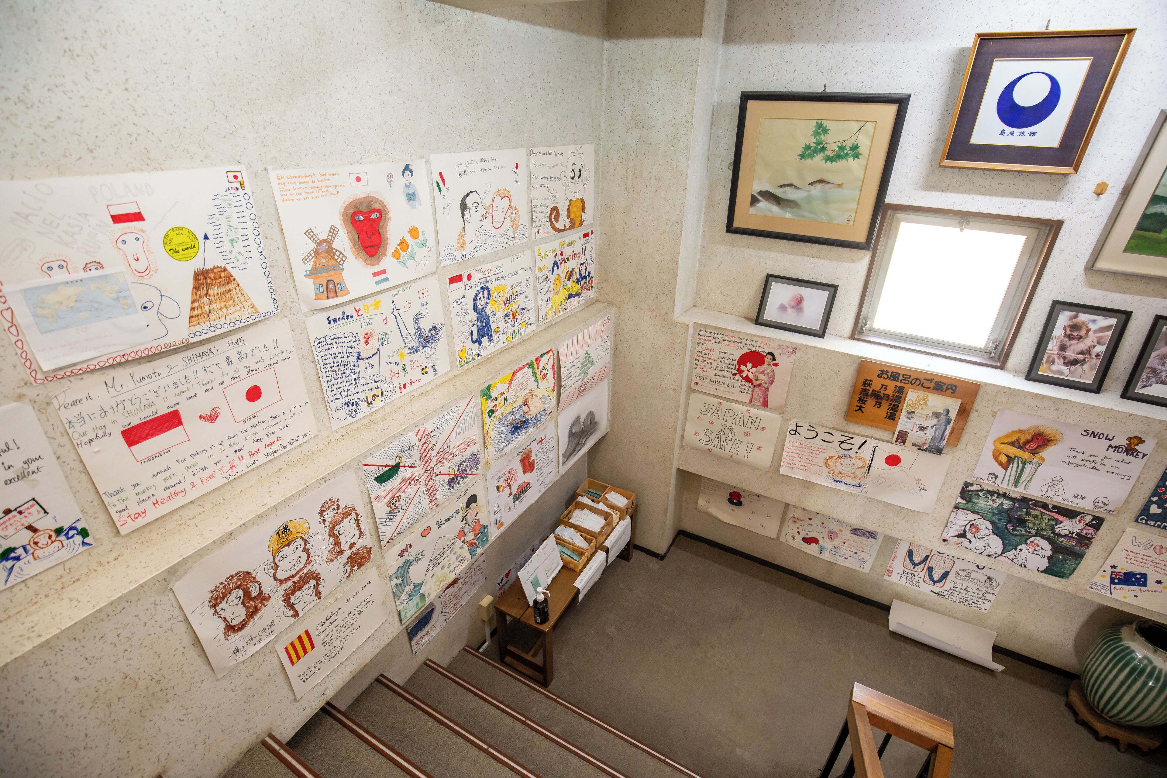 A wall with various drawings and notes, a framed picture of a landscape, and a small wooden stool.