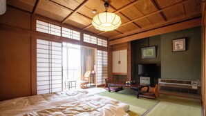 A traditional Japanese room with tatami flooring, a large bed, a television, and sliding doors. - Shimaya (Yamanouchi)