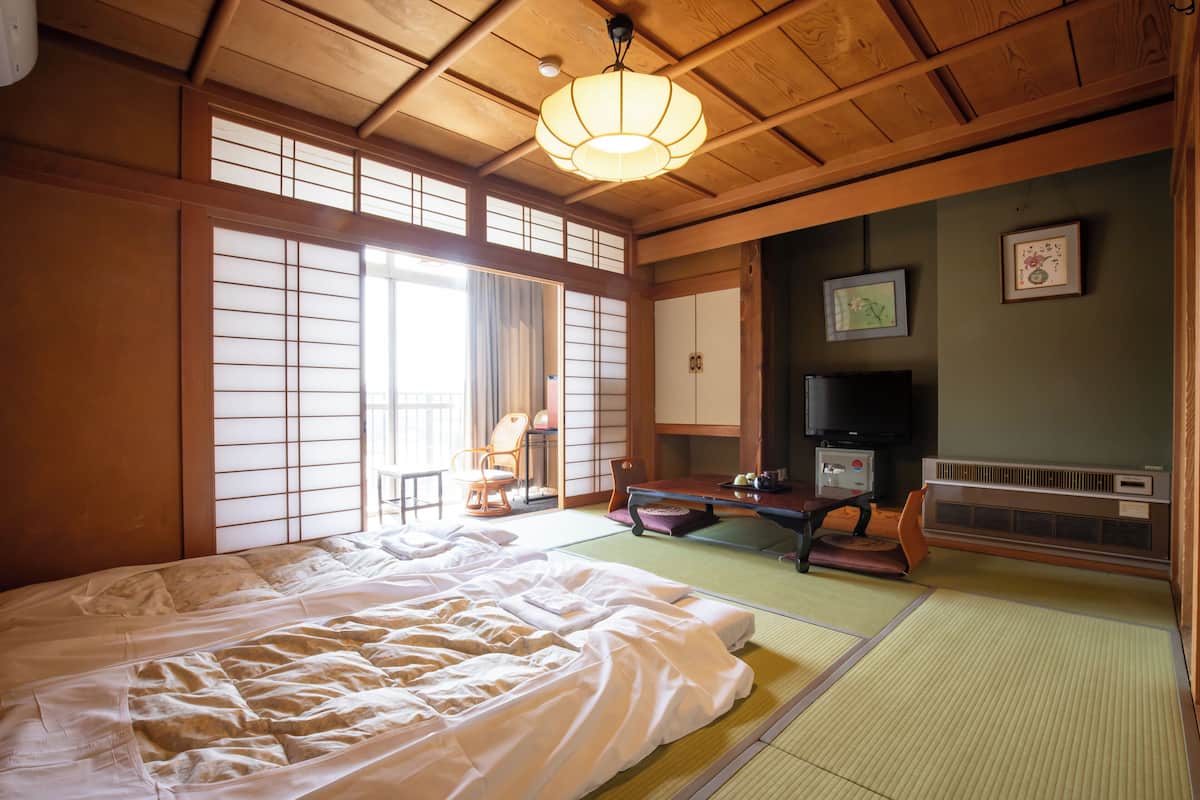 A traditional Japanese room with tatami flooring, a large bed, a television, and sliding doors.