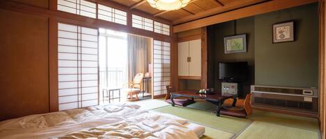 A traditional Japanese room with tatami flooring, a large bed, a television, and sliding doors.