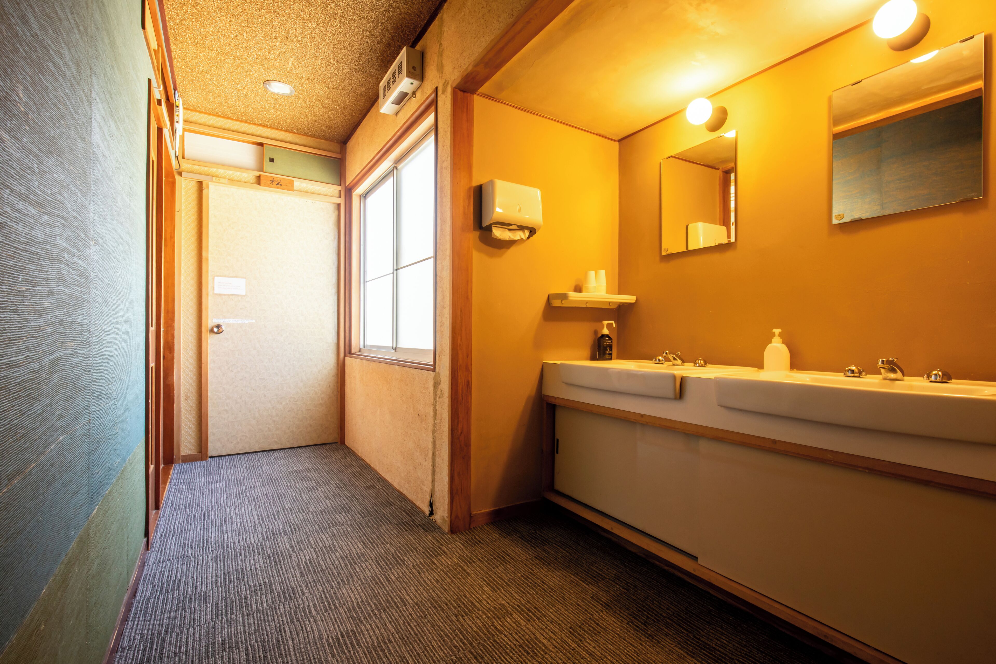 Un bany d'hotel amb un lavabo, mirall i dispensador de tovalloles.