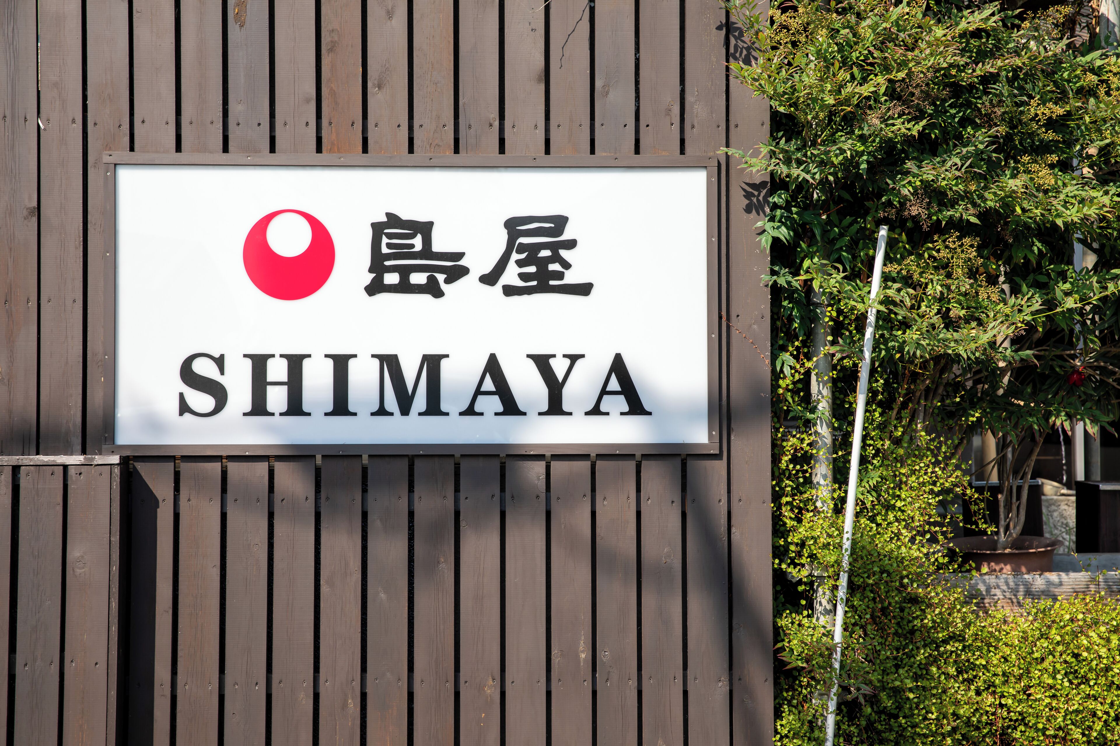 A sign with Japanese characters and the English word 'SHIMAYA' on a wooden wall.
