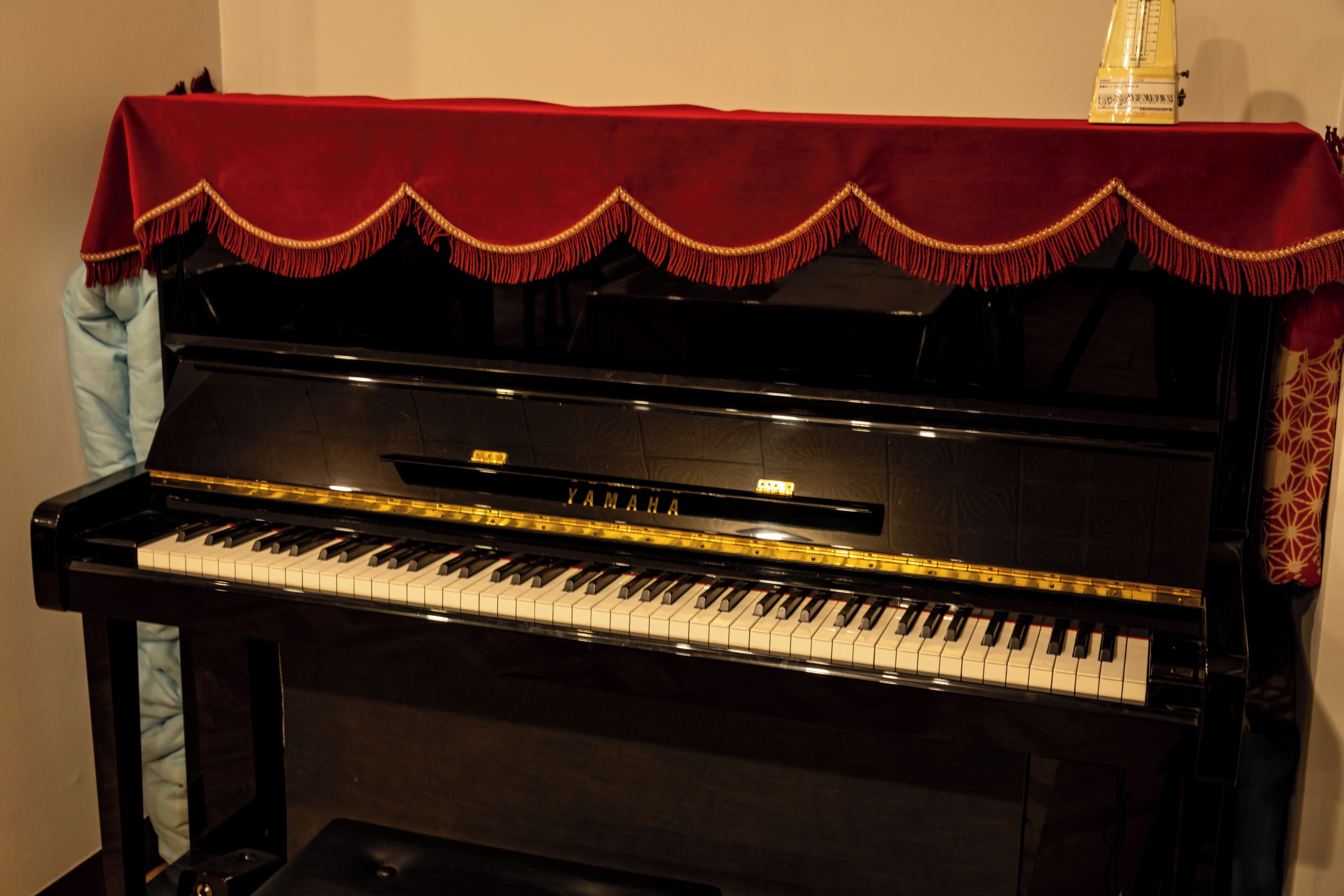 A black Yamaha upright piano with a red cloth on top.