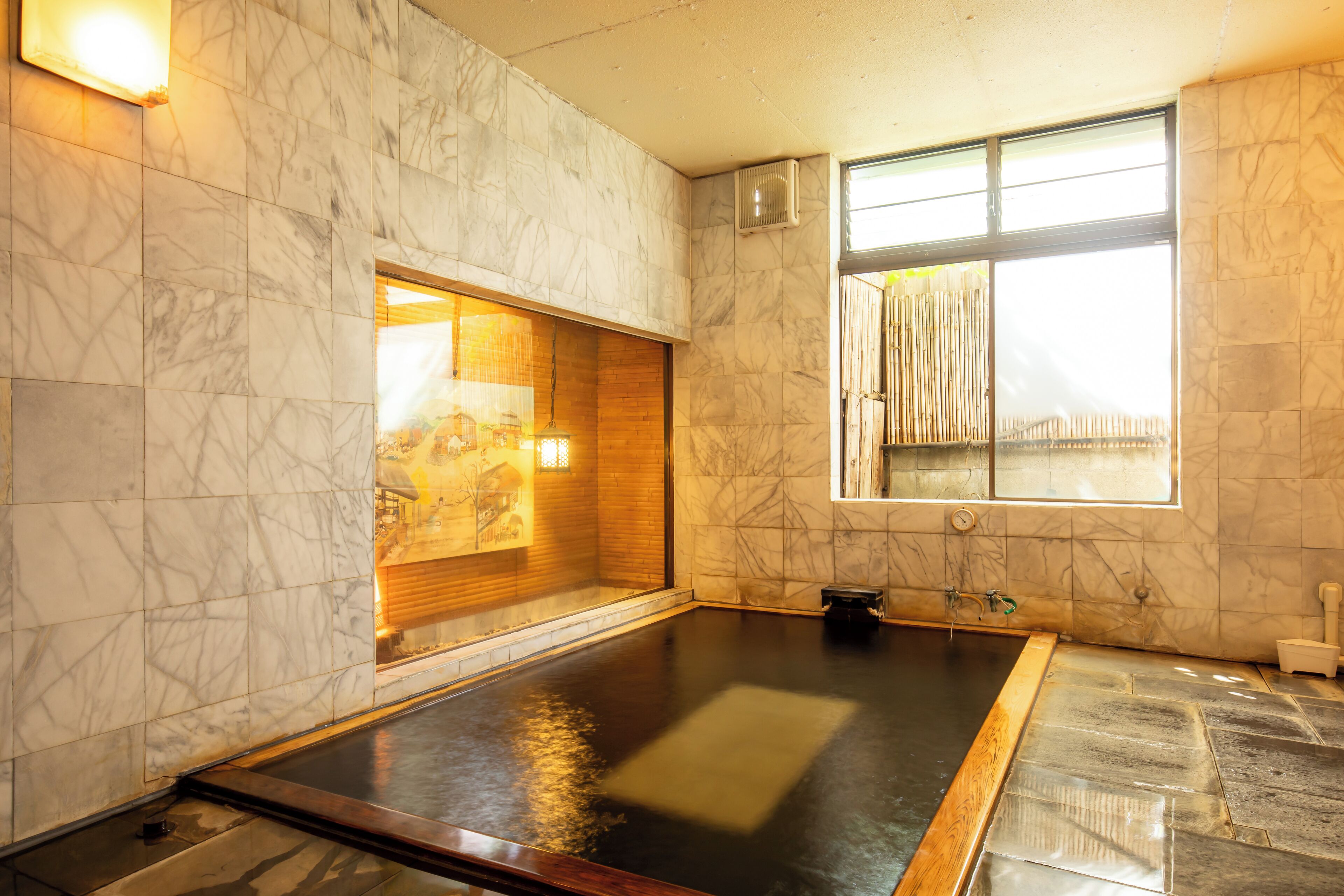 A spa room with a large hot tub, marble walls, and a window with bamboo blinds.