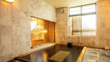 A spa room with a large hot tub, marble walls, and a window with bamboo blinds.