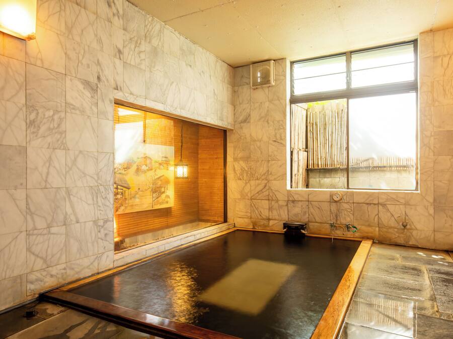 A spa room with a large hot tub, marble walls, and a window with bamboo blinds.