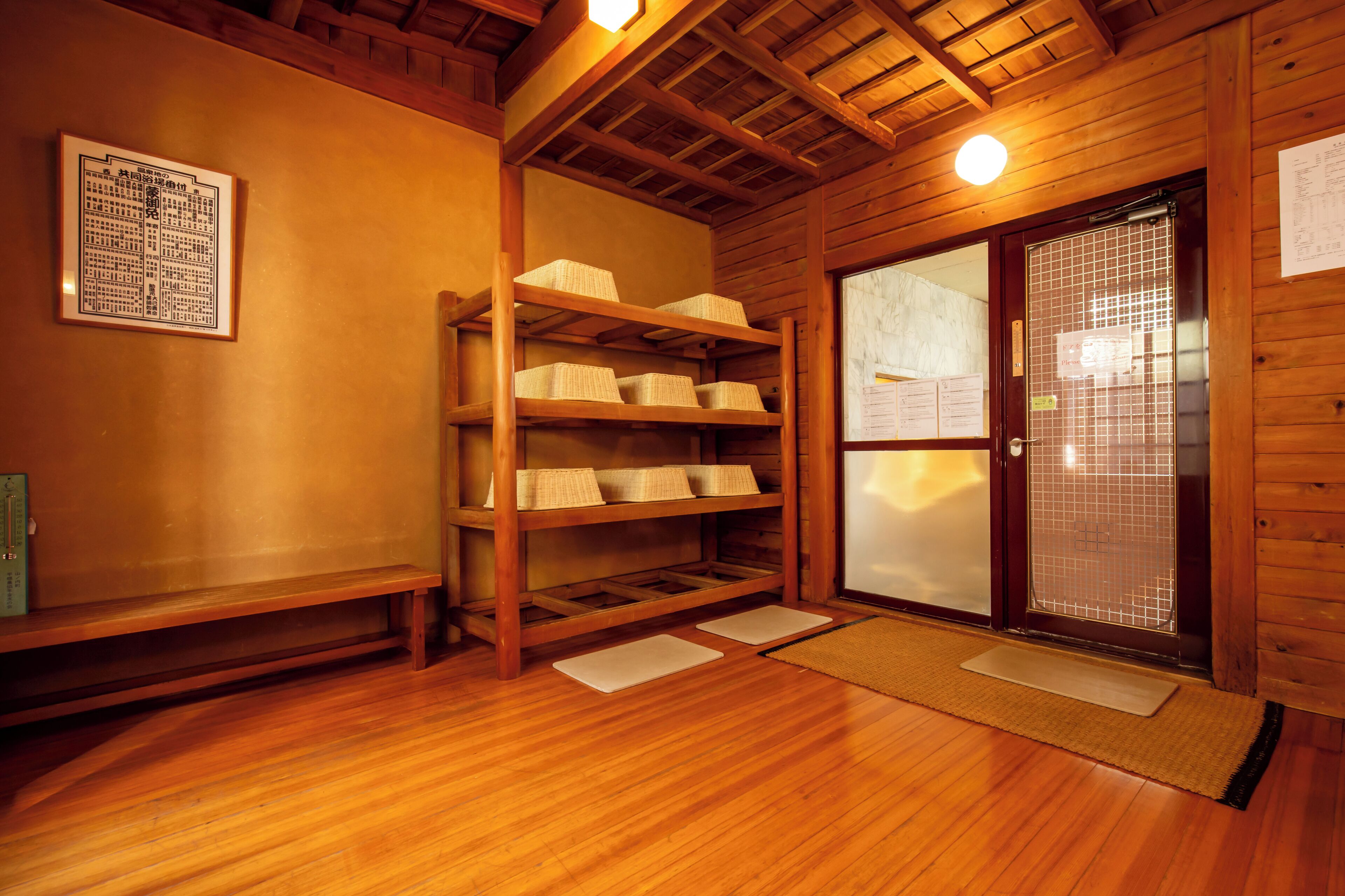 A wooden interior with a wooden shelf holding woven baskets, a wooden bench, and a sliding glass door with a metal grid.