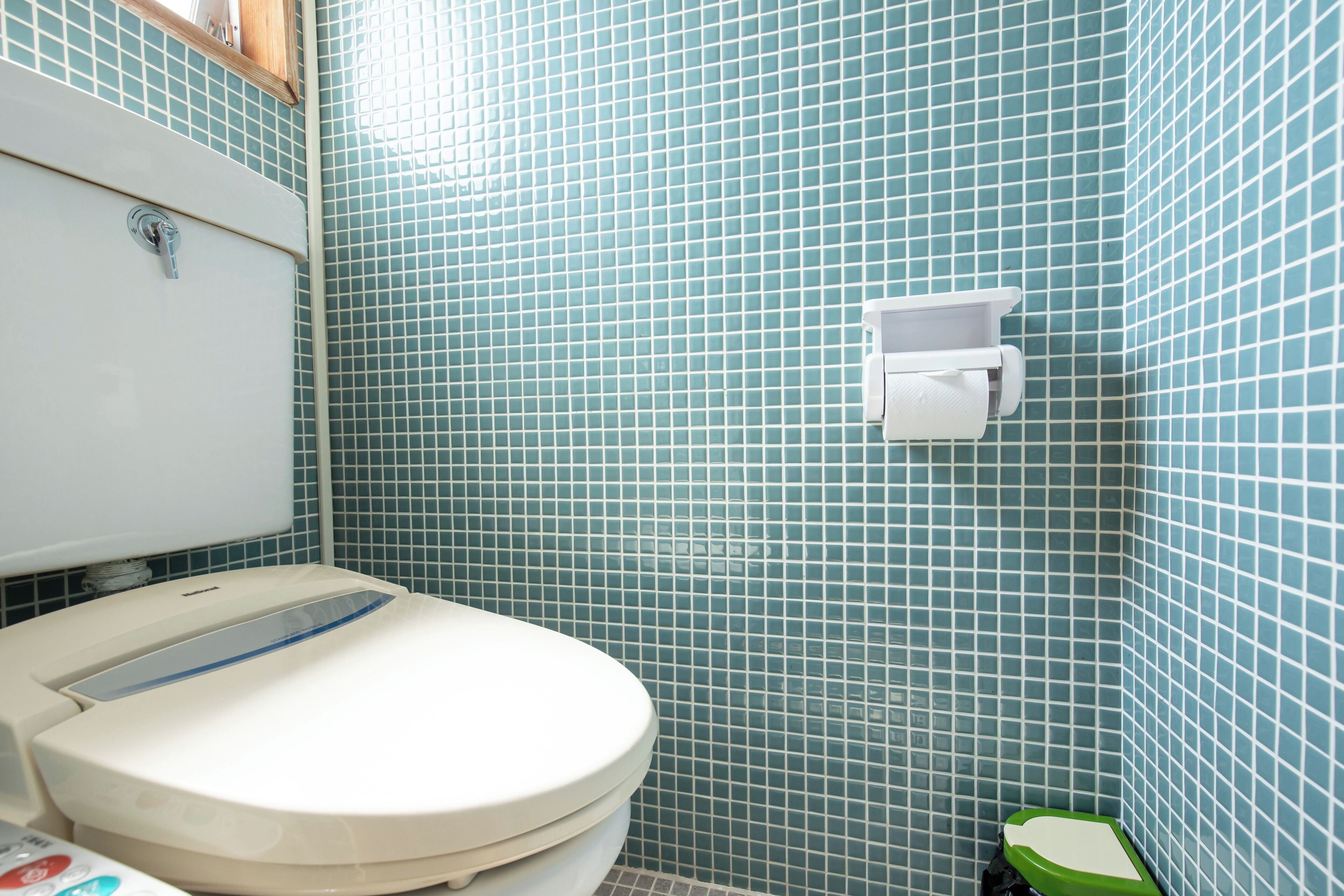 Une salle de bain équipée de toilettes, d’un distributeur d’essuie-tout et d’une poubelle verte.