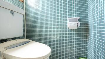Une salle de bain équipée de toilettes, d’un distributeur d’essuie-tout et d’une poubelle verte.