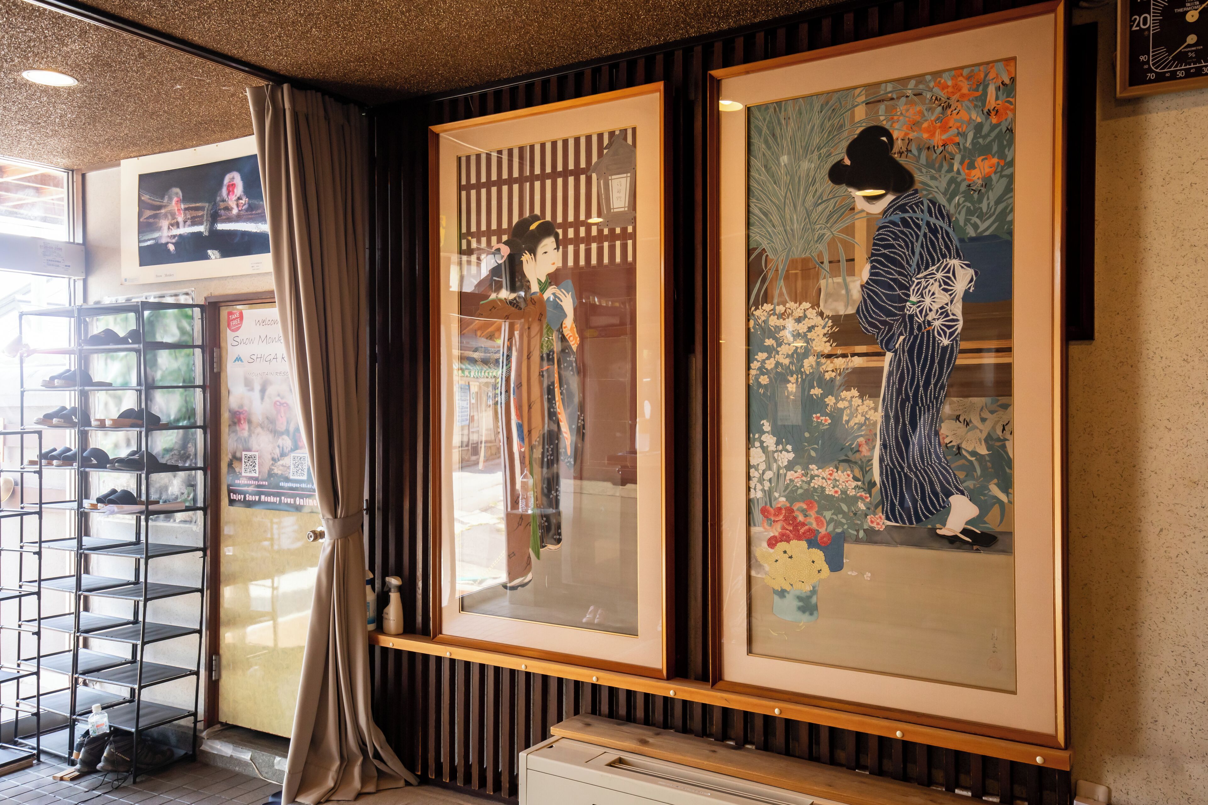 A room with traditional Japanese artwork, a shoe display, and a wooden floor.