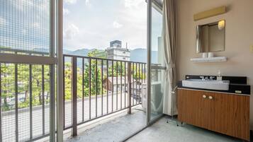 A balcony with a metal railing, a wooden vanity with a mirror and sink, and a view of buildings and trees.