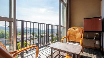 Un balcón con una mesa y dos sillas de mimbre, con vistas panorámicas a una ciudad y montañas.