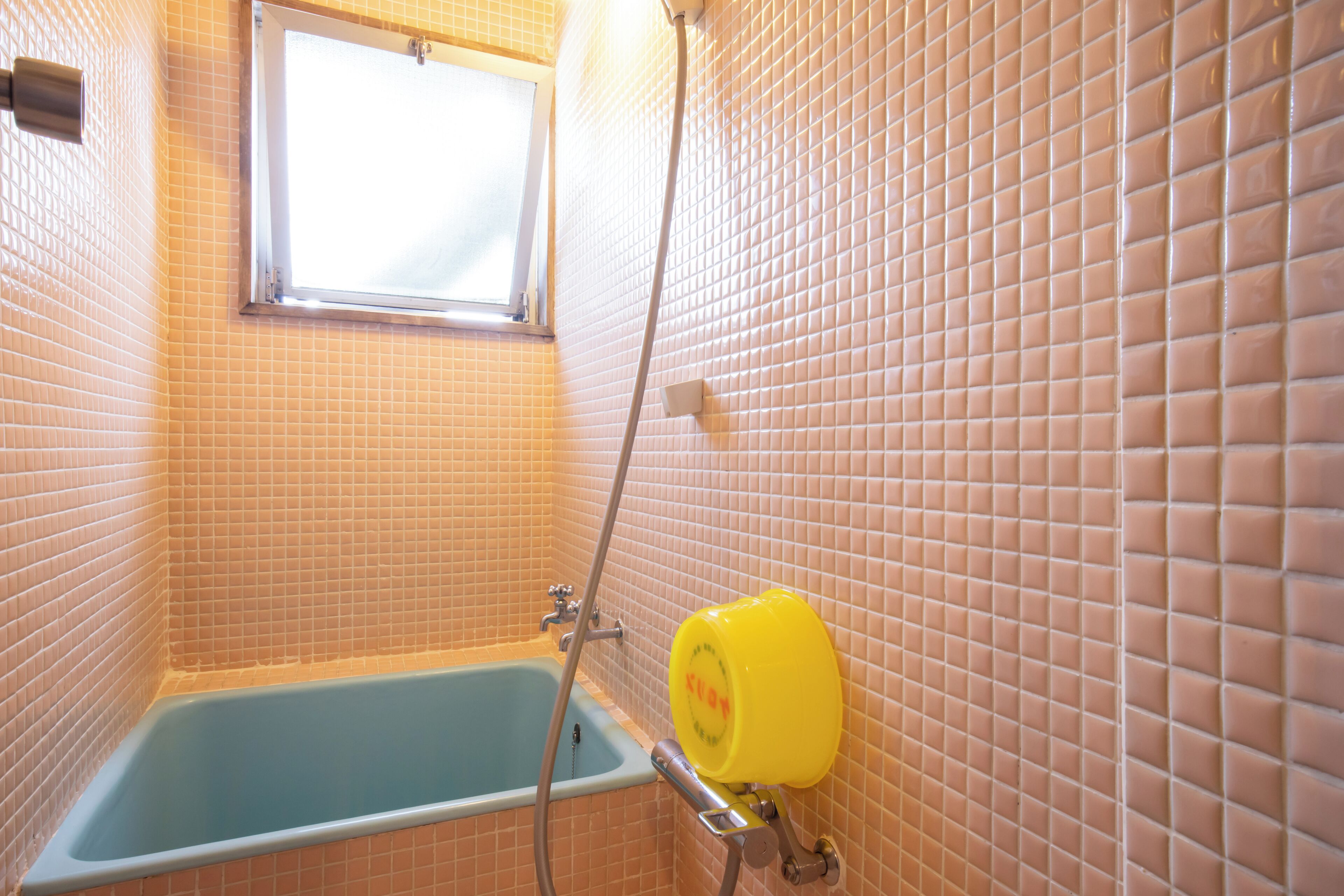 Une salle de bain avec une baignoire, une fenêtre et un chauffe-eau jaune.