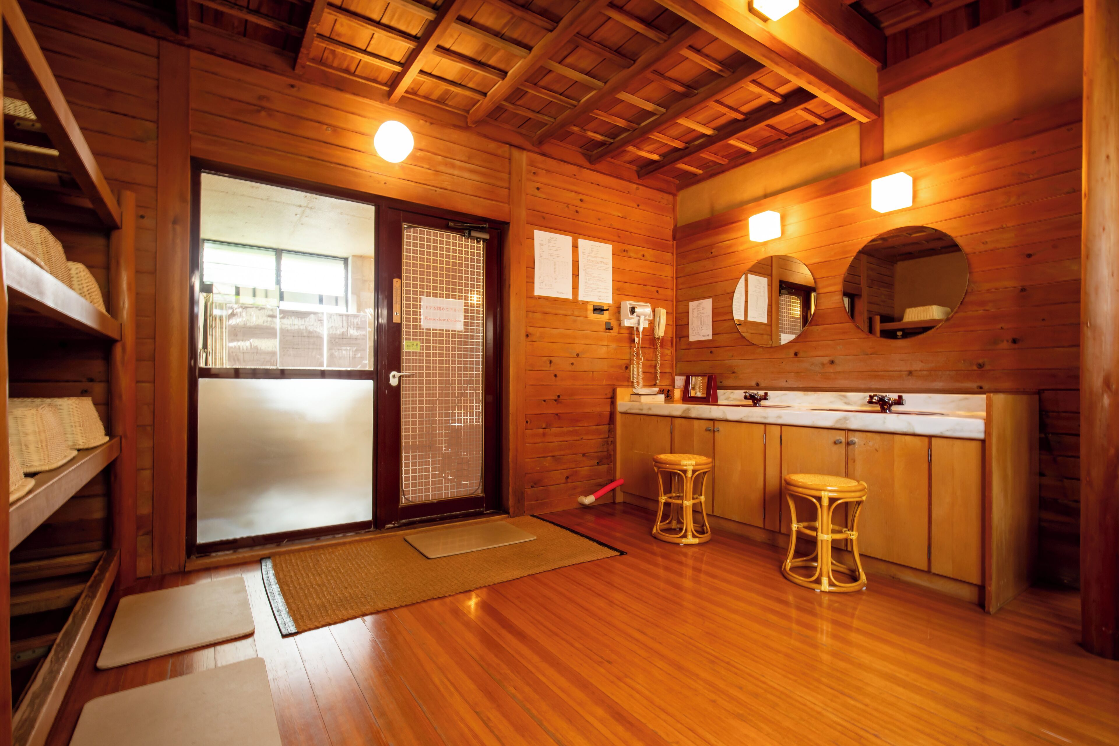 A wooden interior with a sliding glass door, wooden cabinets, a sink, and two stools.