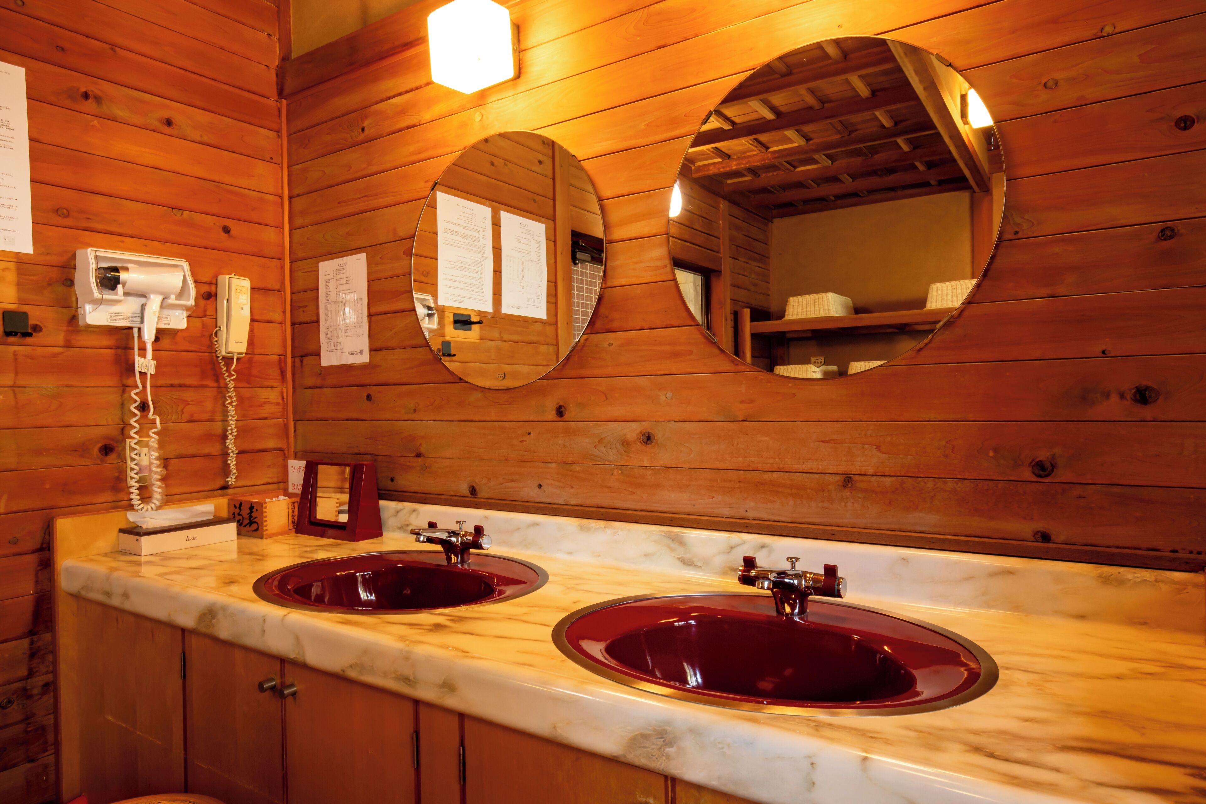A wooden cabin bathroom with two sinks, a telephone, and two mirrors.