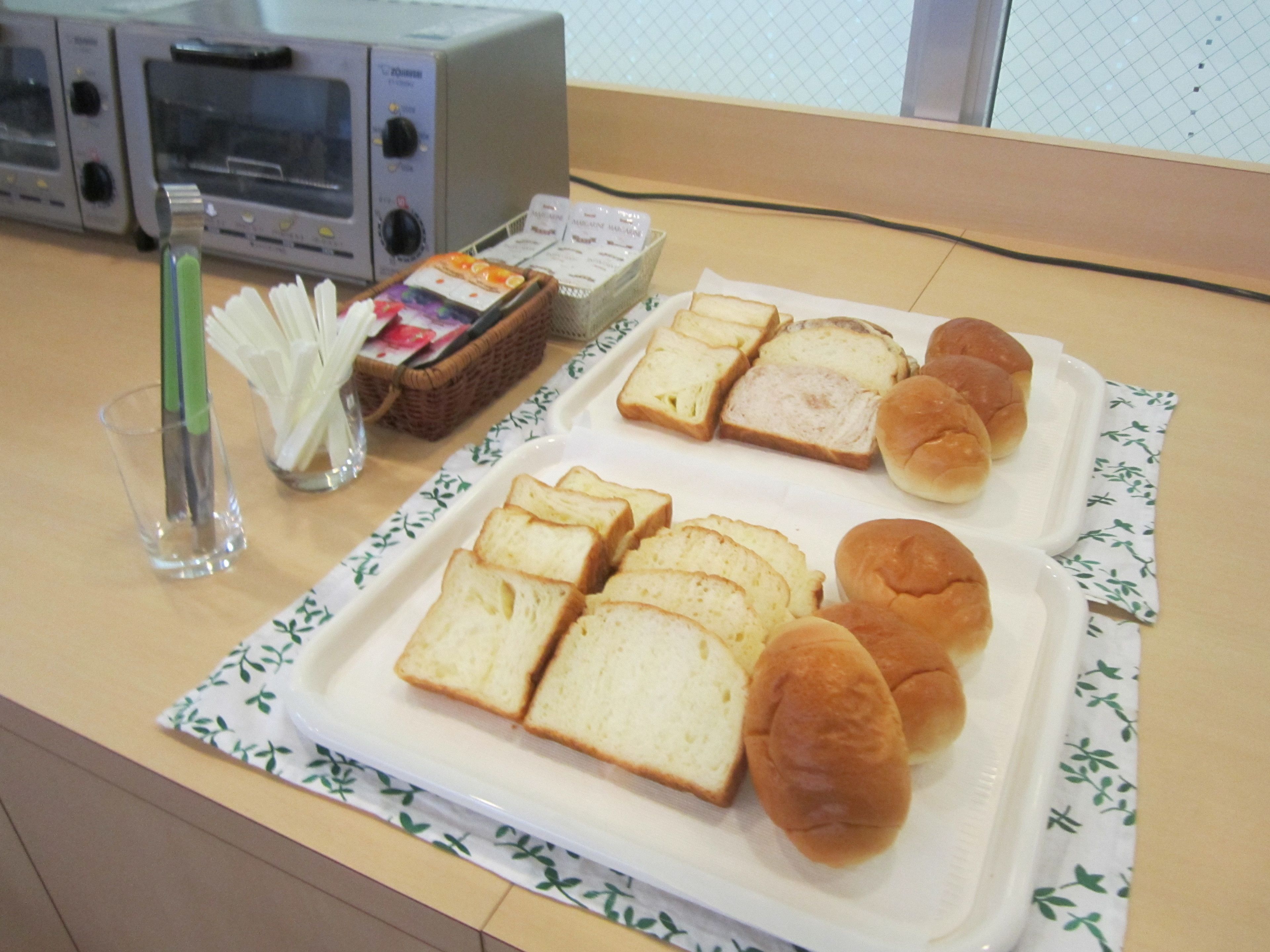 A breakfast tray with bread and rolls on a table with a microwave and a basket of condiments.