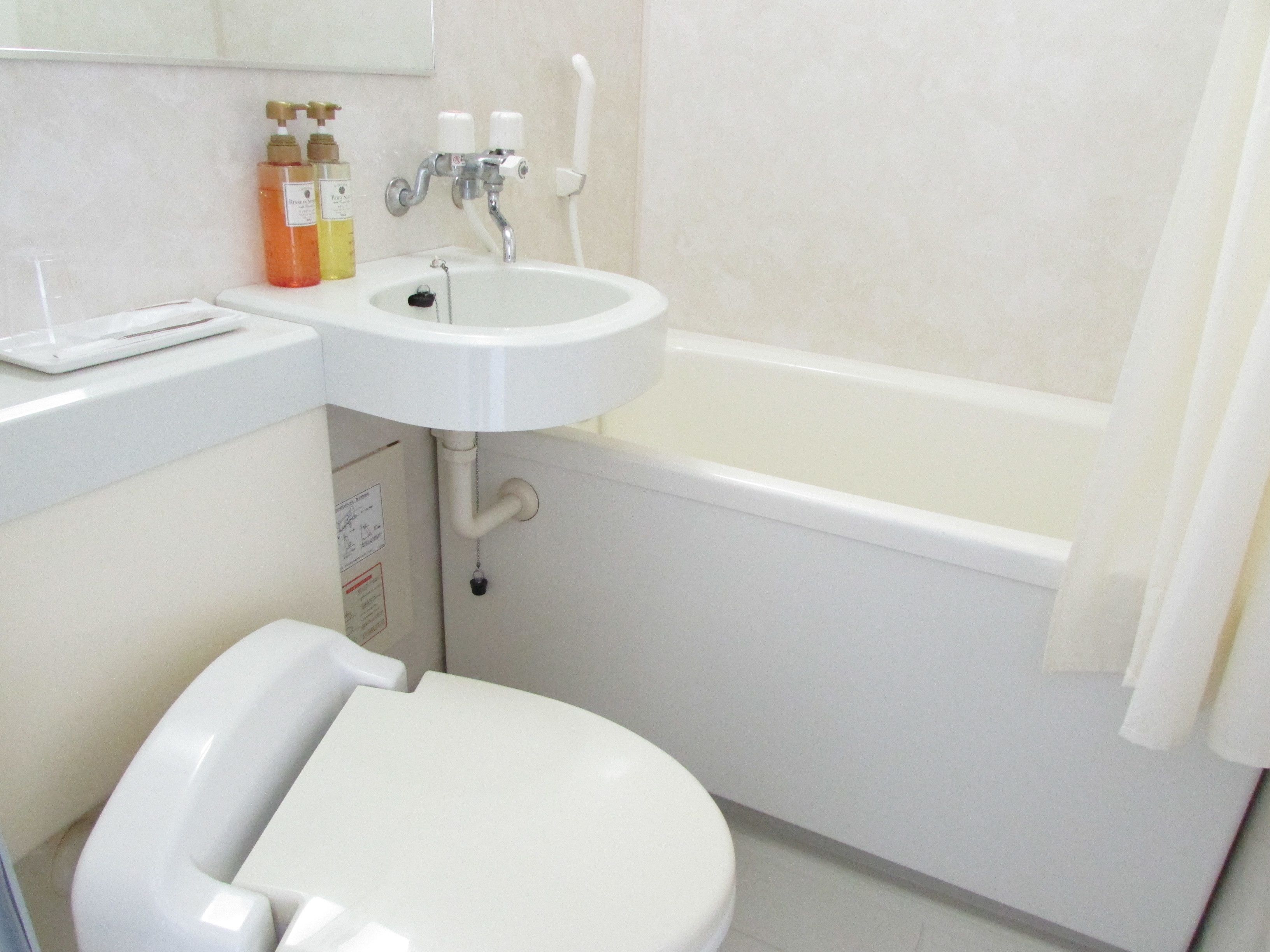 A bathroom with a white sink, toilet, and bathtub. There are toiletries on the sink counter.