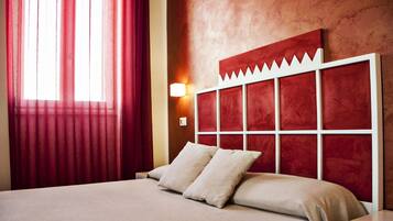 Quarto de hotel com uma cama grande, cortinas vermelhas, cabeceira vermelha e uma luminária fixada na parede.
