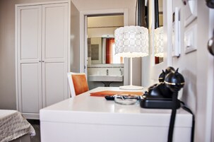 Habitación de hotel con tocador blanco, espejo, lámpara y teléfono.